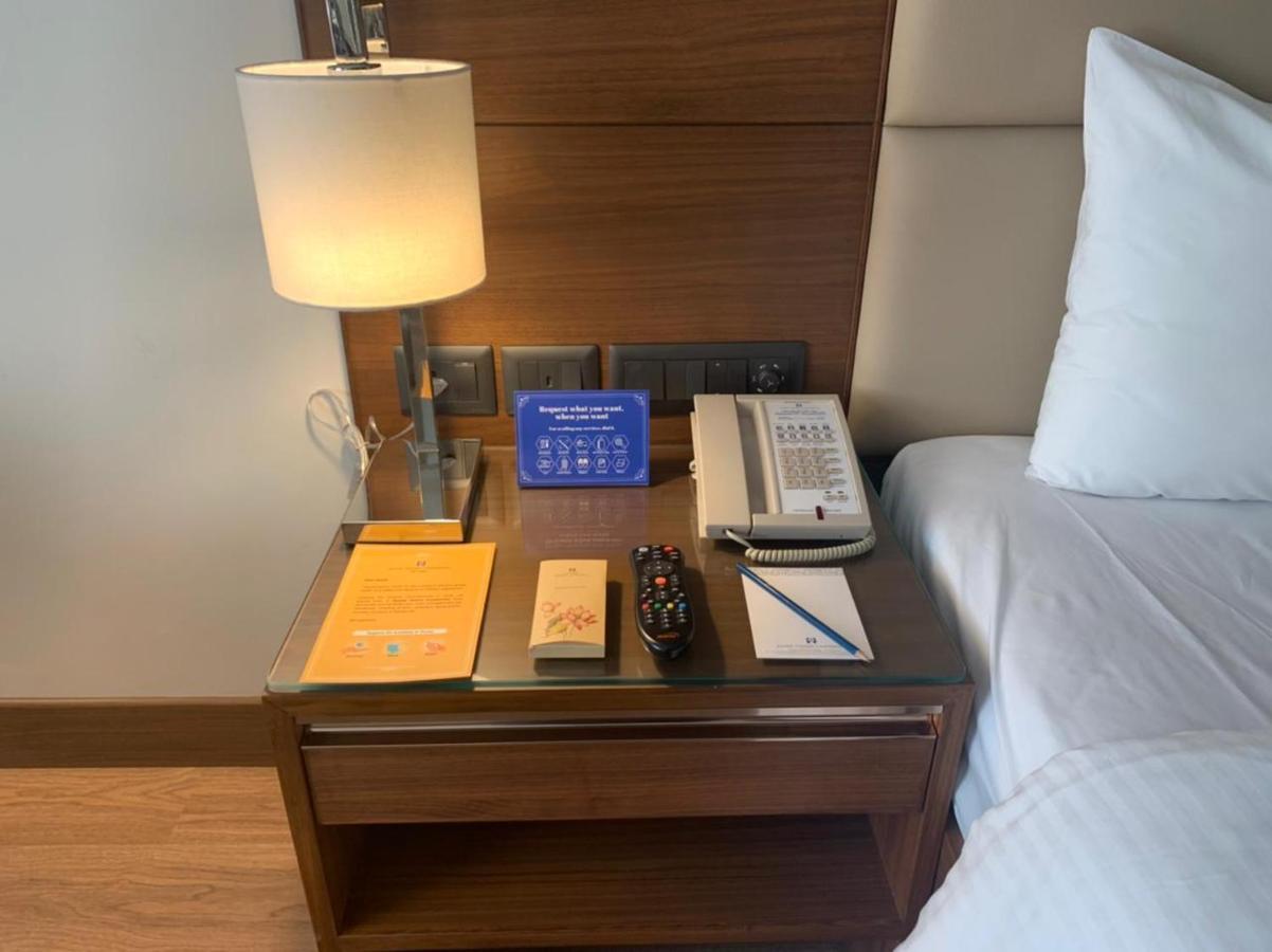 Jaypee Vasant Continental Hotel New Delhi Luaran gambar A bedside table with a telephone, a lamp, a pen and a notepad